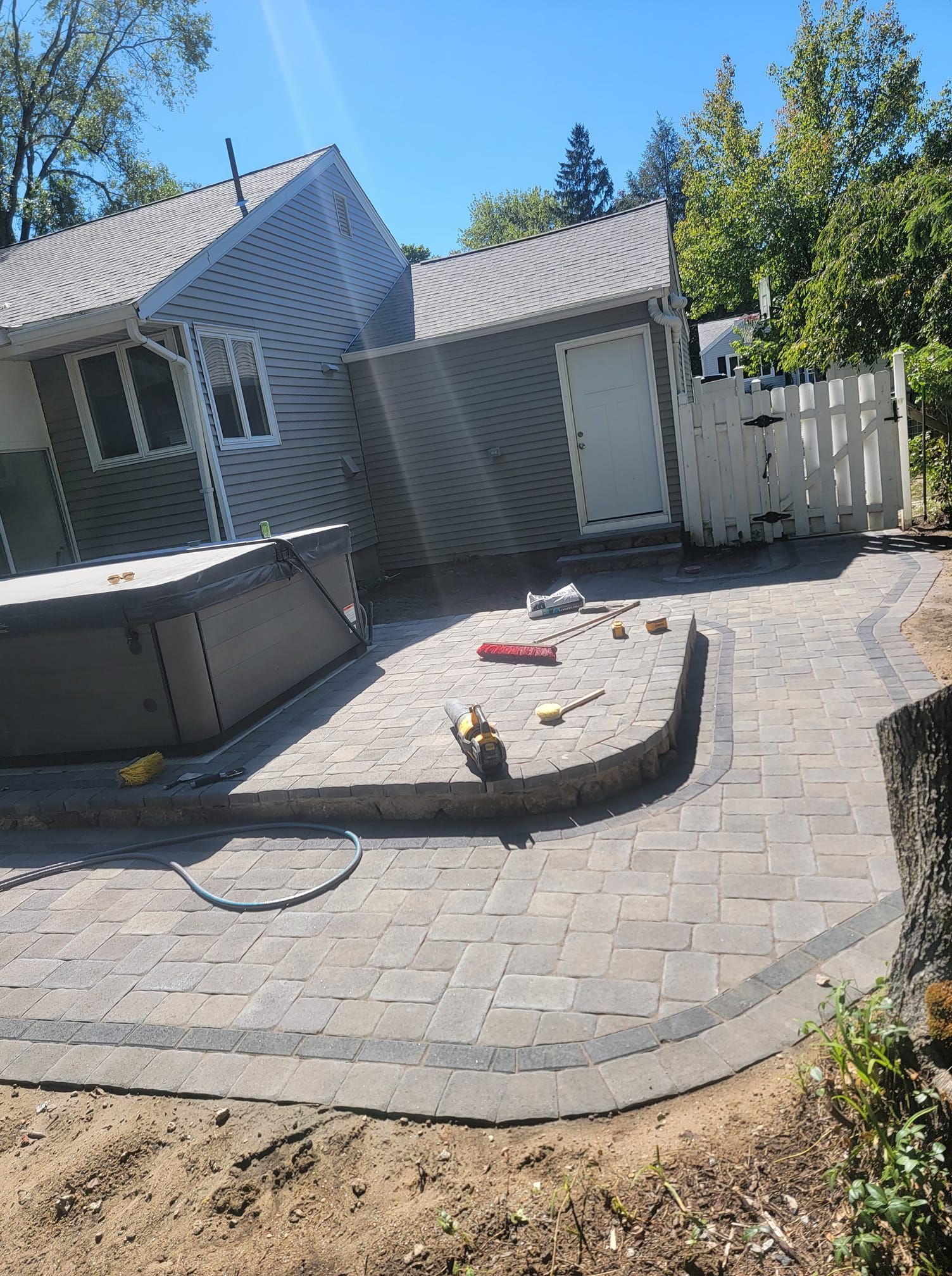 Paver patio with hot tub next to a house and shed on a sunny day.