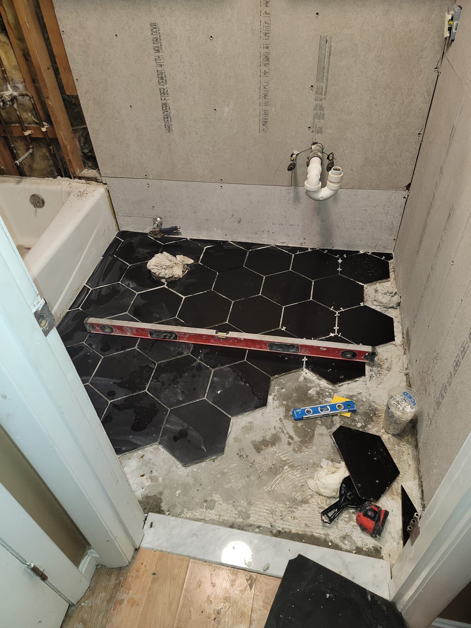 Bathroom floor tile installation in progress: black hexagon tiles, level, partially tiled floor.