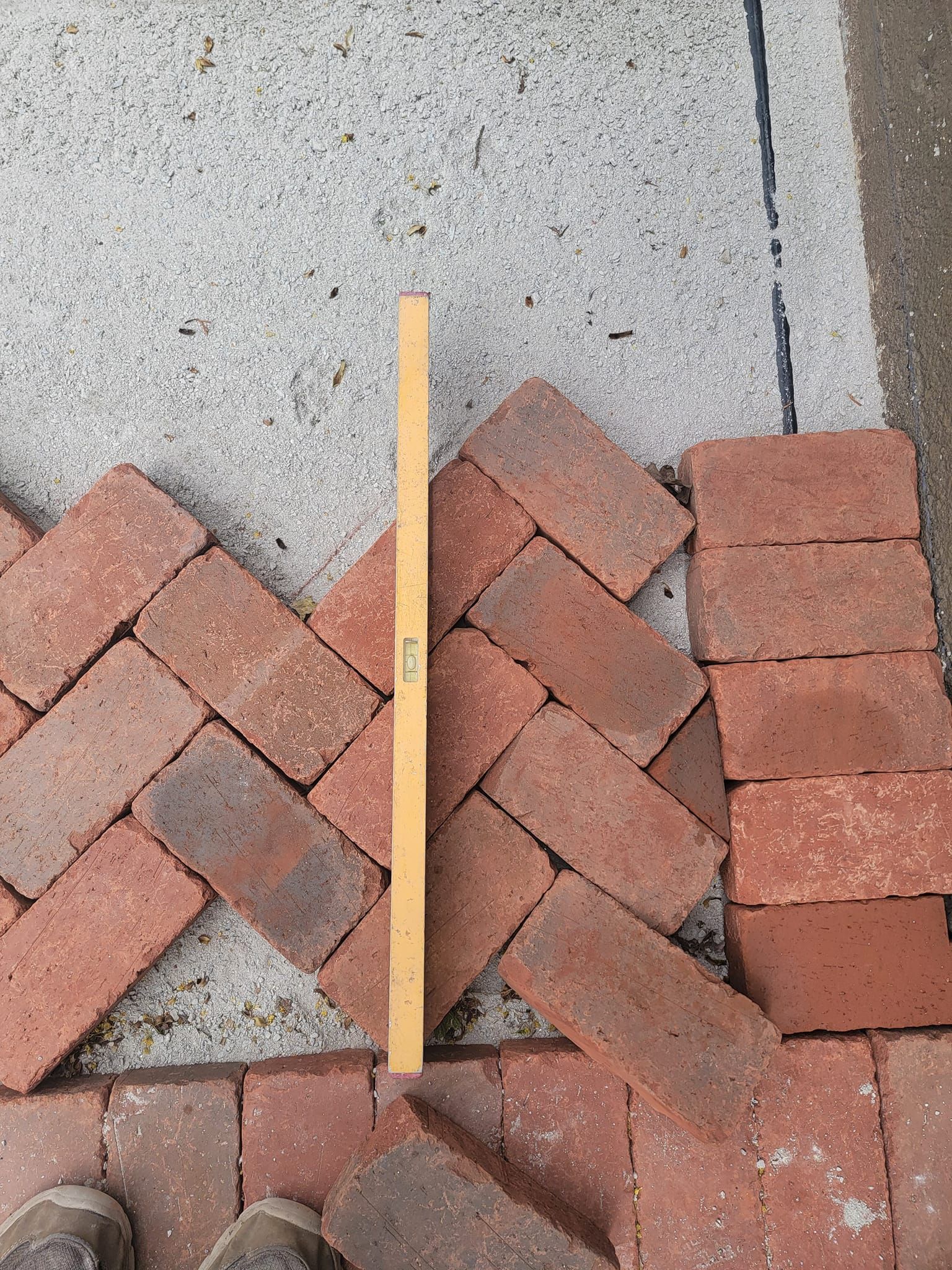 Bricks in a herringbone pattern being laid on concrete, checked with a level.