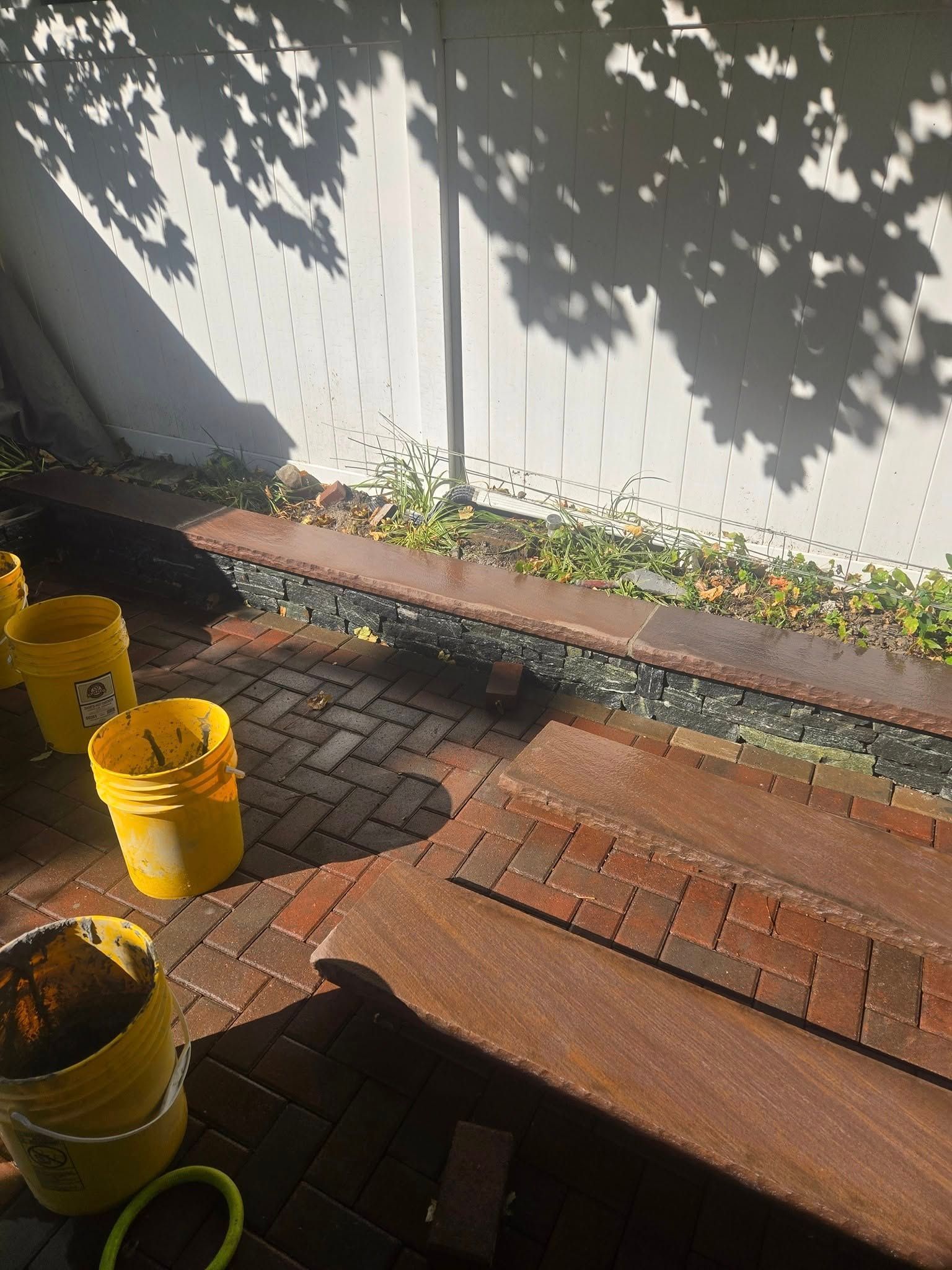 Brick patio with a wooden table, several yellow buckets, and a retaining wall.