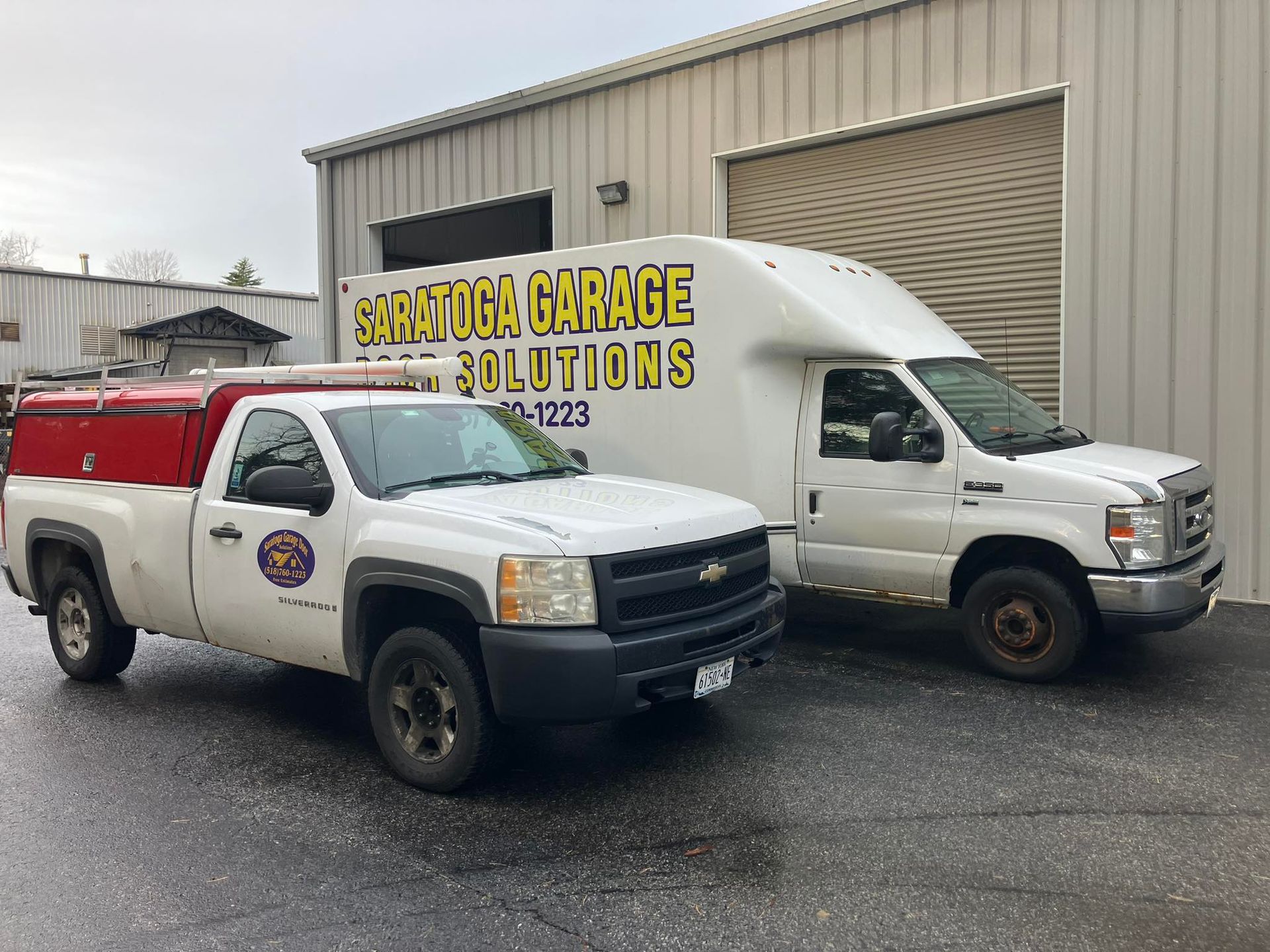White pickup truck and service van parked outside a garage, both labeled