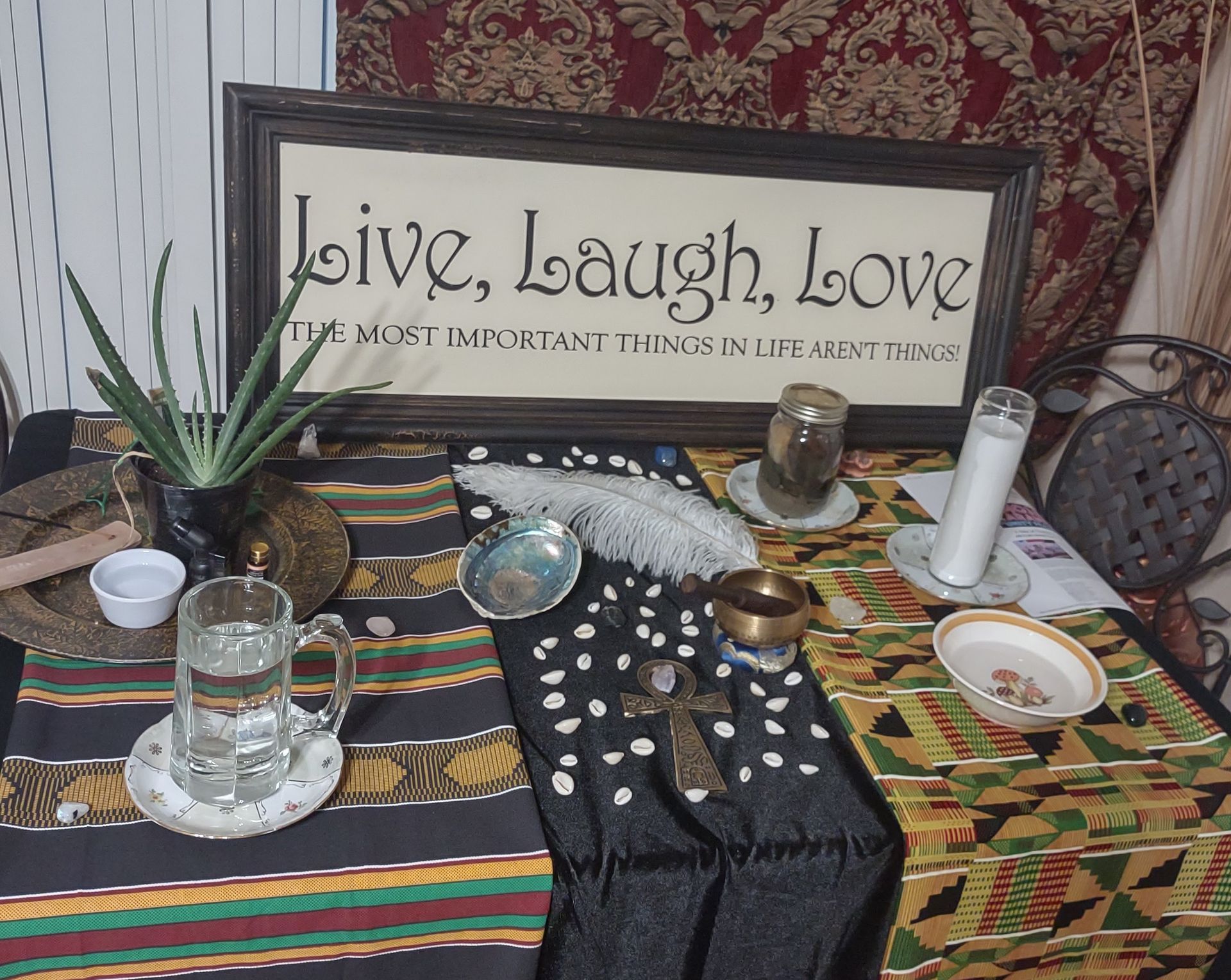 Decorative altar with framed “Love, Laugh, Love” sign, candles, crystals, incense, and patterned cloth on a table
