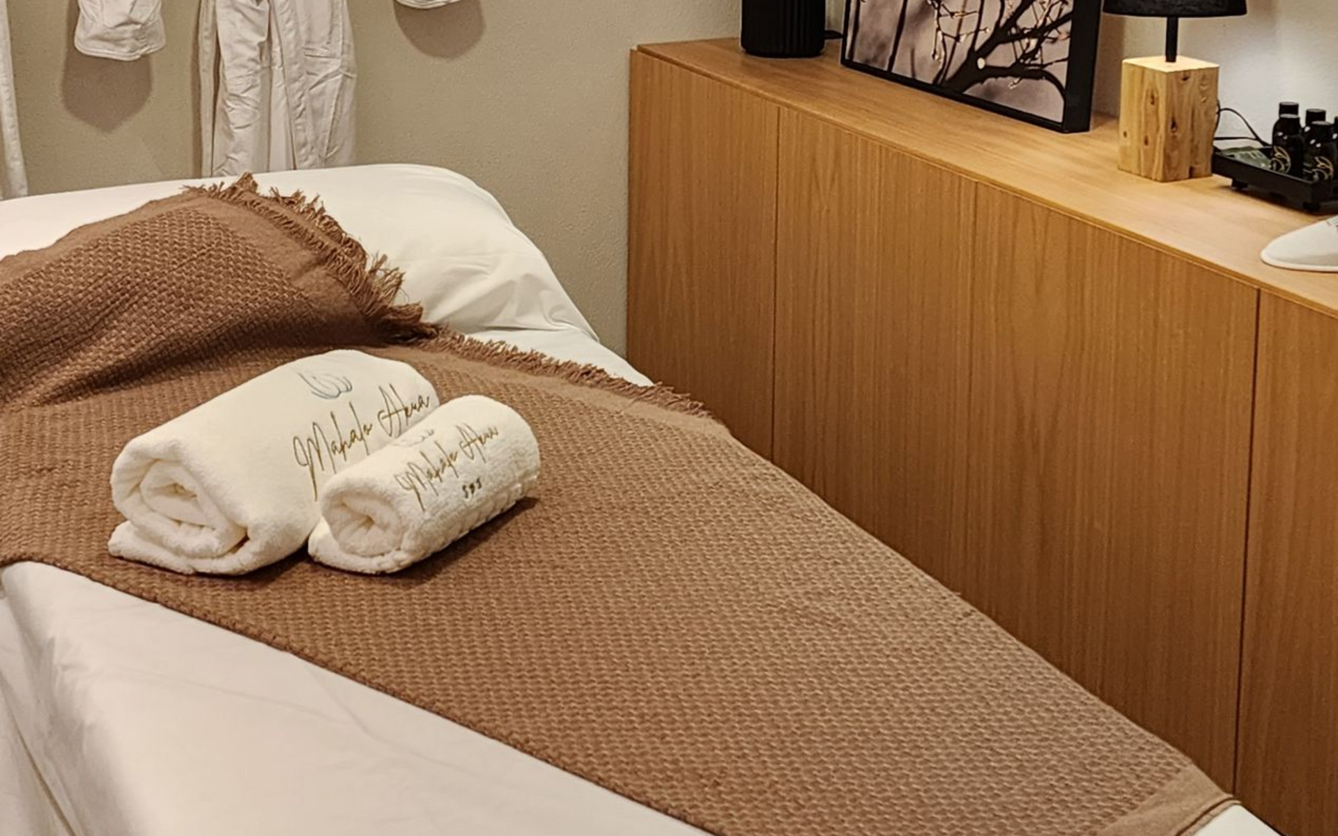 Cama arrumada com roupa de cama marrom e branca ao lado de uma cômoda de madeira em um quarto aconchegante.