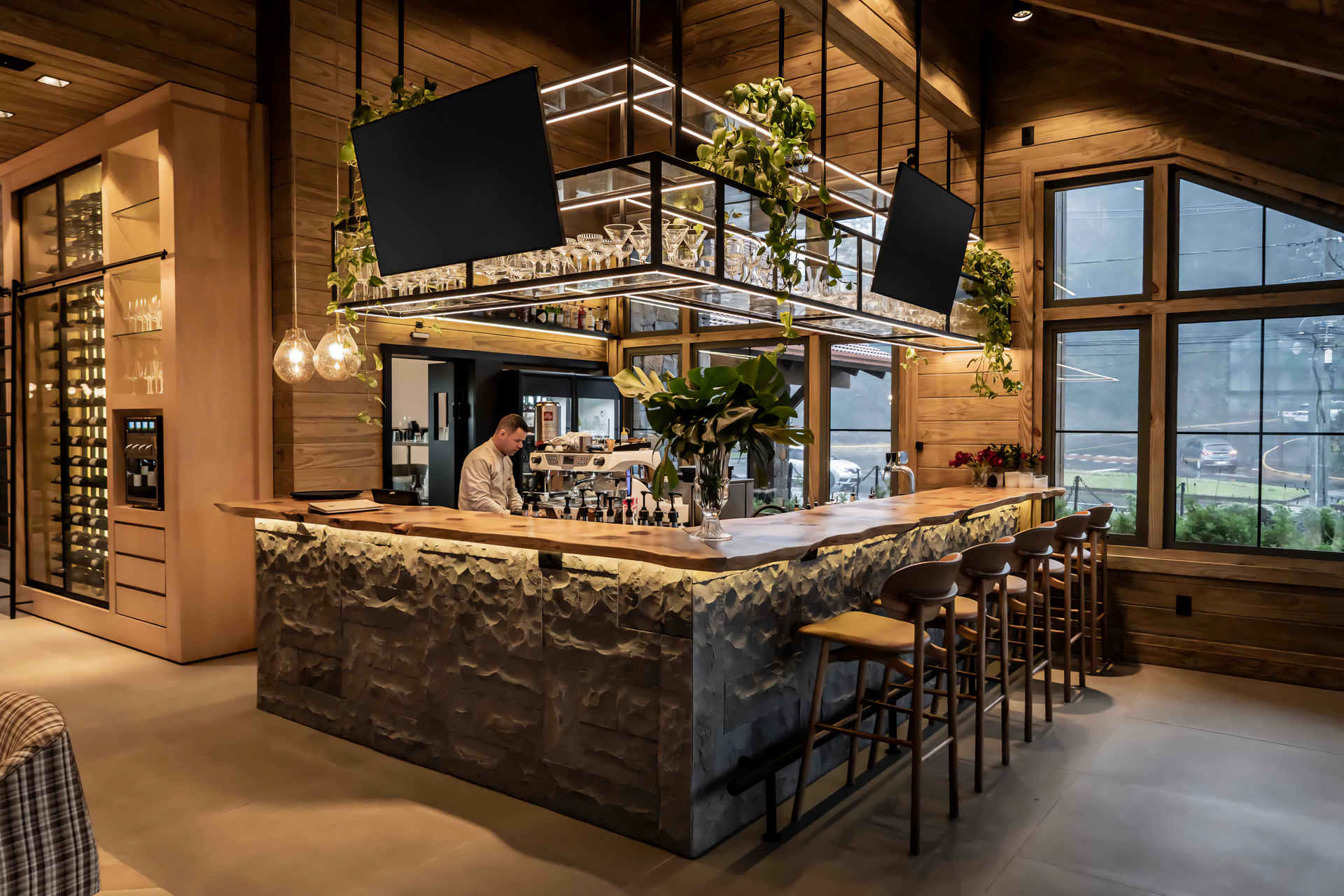 Bar de restaurante elegante com luzes pendentes, balcão de pedra e banquetas altas em um interior moderno com painéis de madeira.