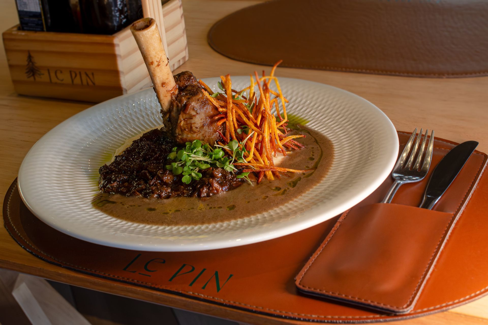 Prato gourmet empratado com molho e guarnição em uma mesa de restaurante com talheres e cardápio de couro.