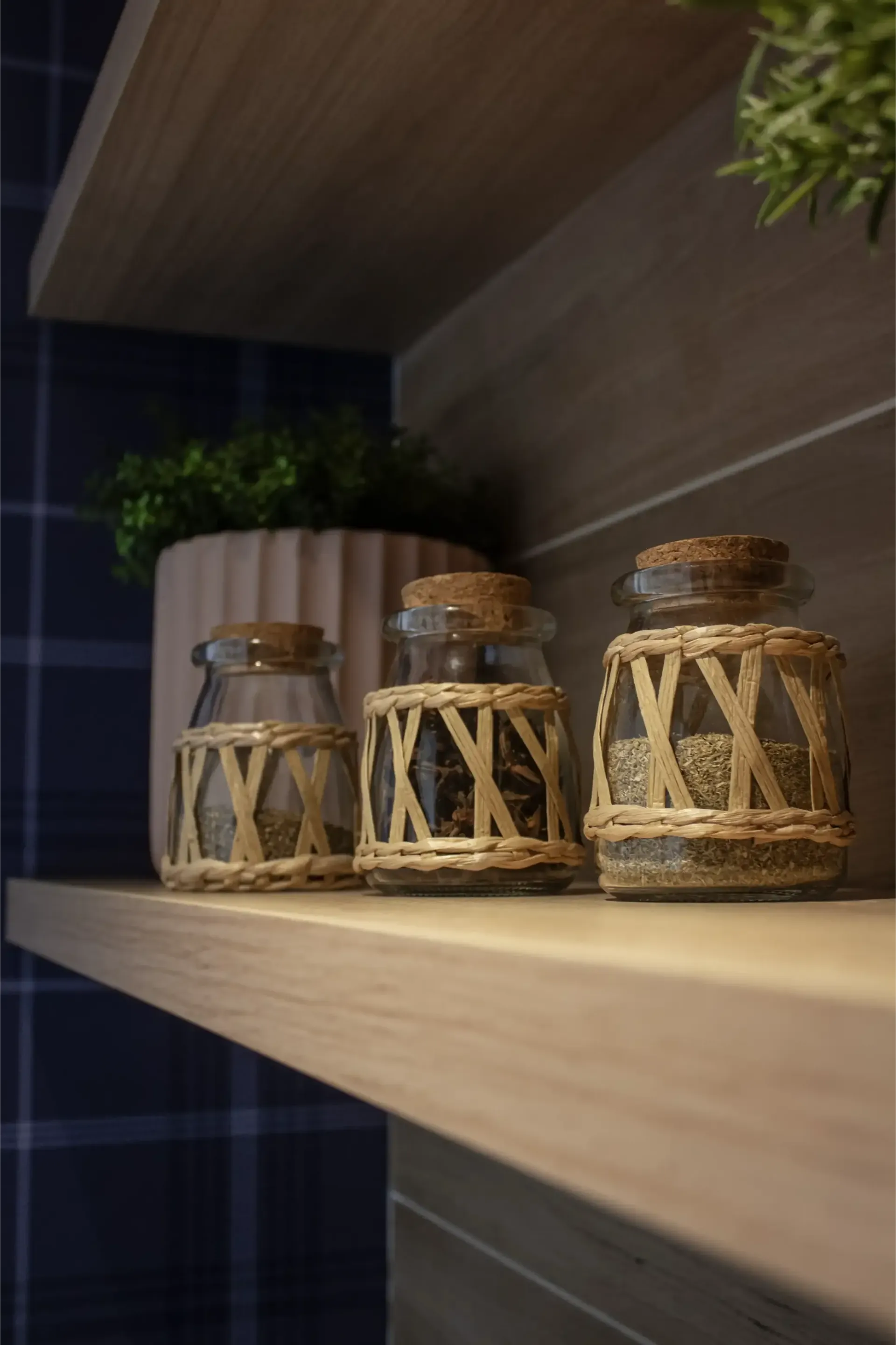 Três pequenos potes de vidro decorativos com revestimento de vime trançado sobre uma prateleira de madeira.