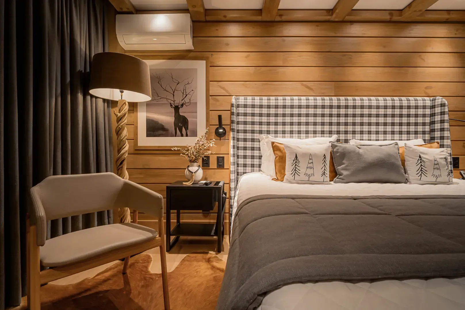 Quarto aconchegante com cabeceira xadrez, cama bege, poltrona, abajur e paredes com painéis de madeira.