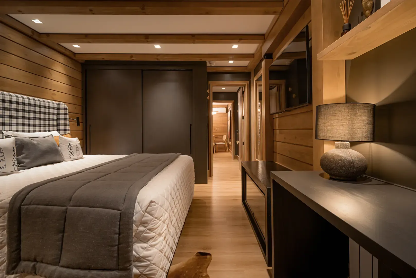 Quarto moderno com painéis de madeira, cama, armários embutidos e iluminação aconchegante.