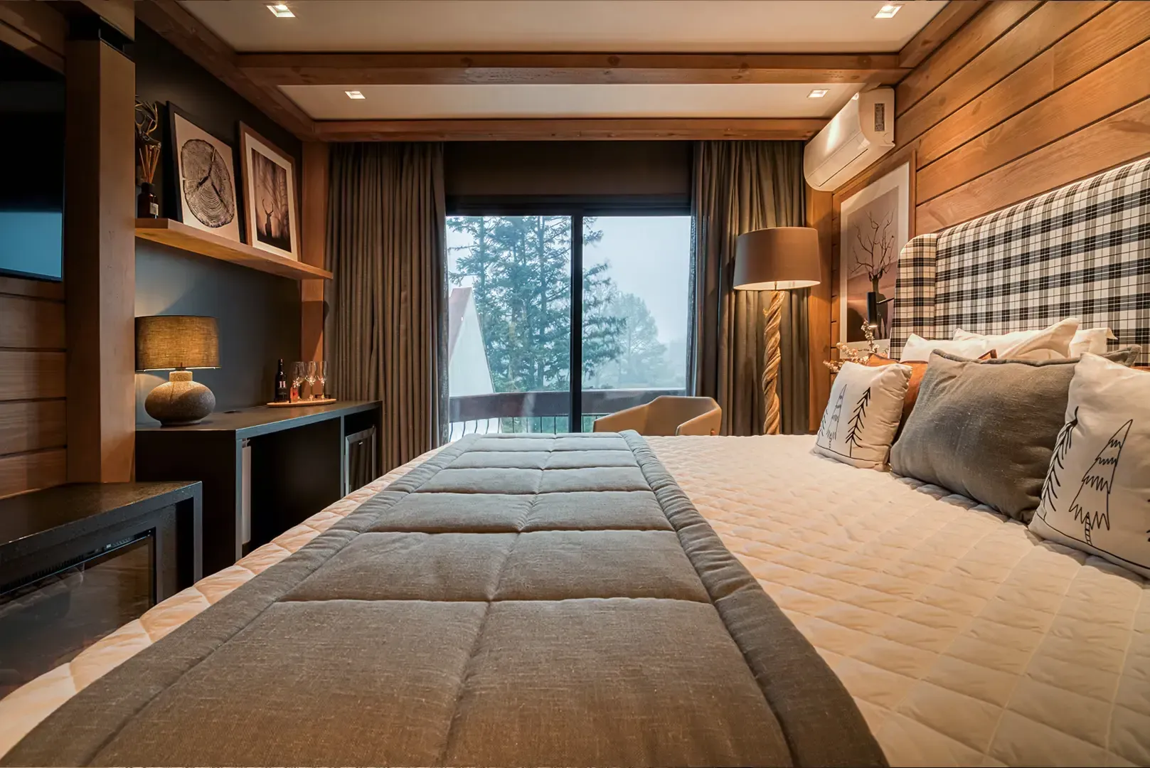 Quarto moderno com uma cama grande, paredes revestidas de madeira e vista da janela para árvores cobertas de neve.