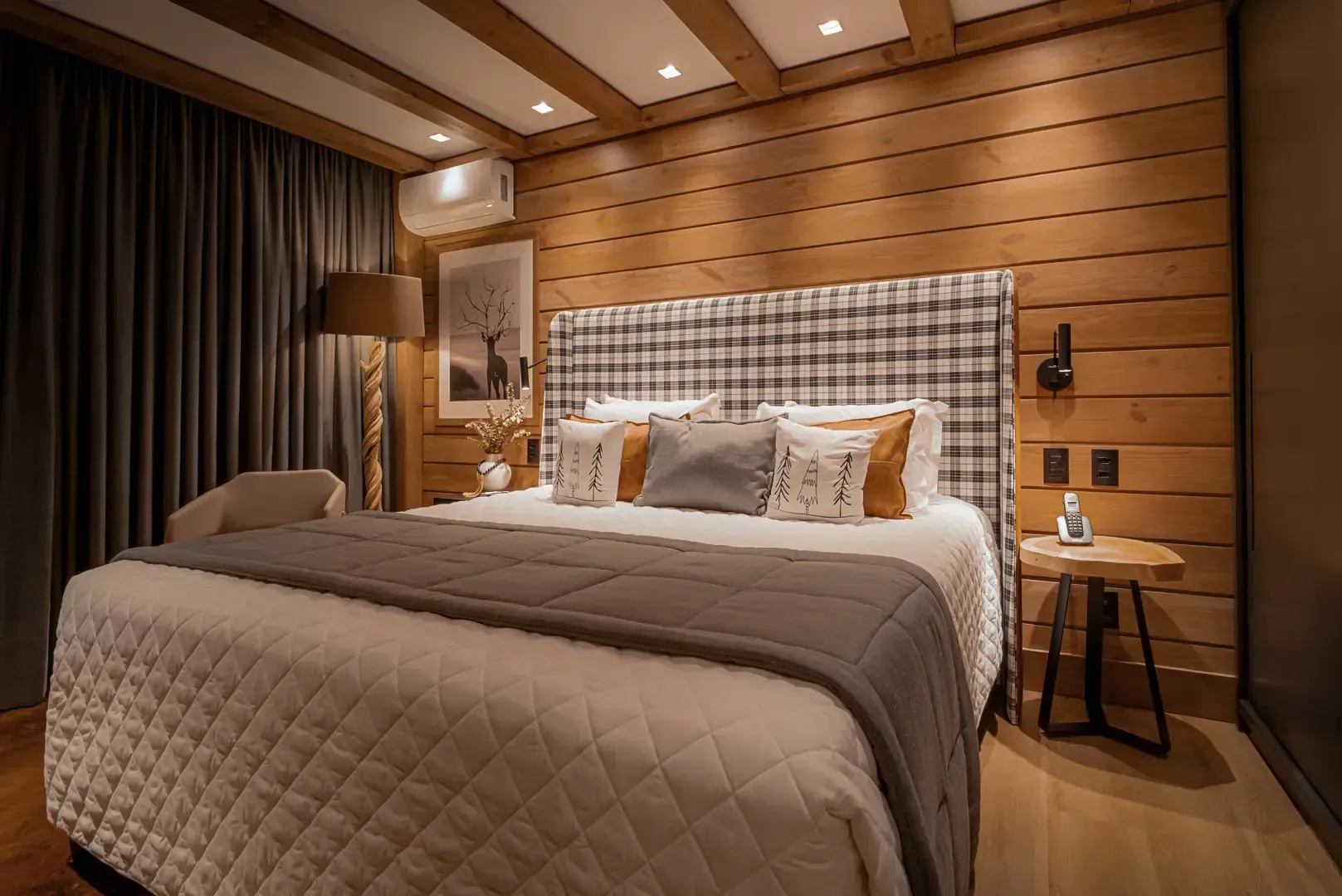Quarto moderno com cama acolchoada, paredes de madeira em tons quentes e abajures.