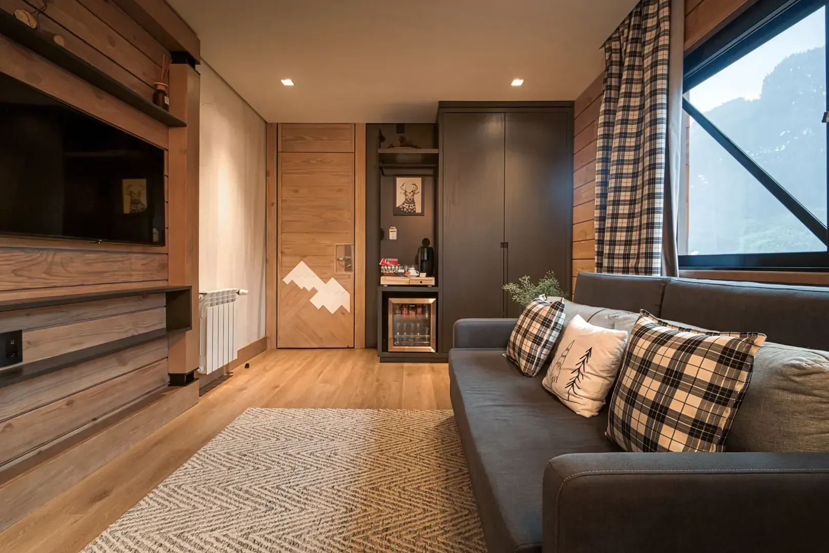 Sala de estar moderna com sofá cinza, almofadas estampadas, tapete de fibras naturais, painéis de madeira e janela ampla.