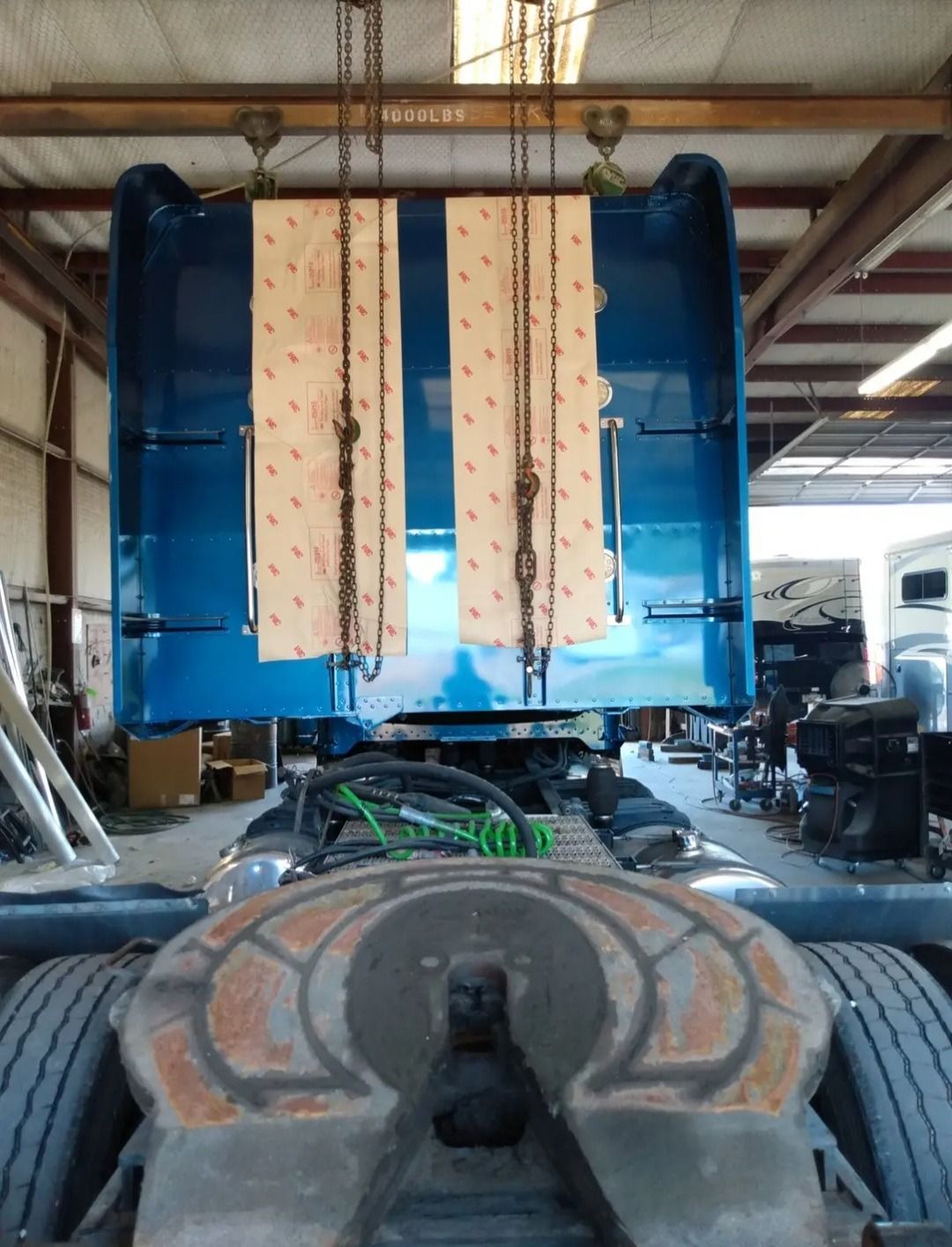 Blue truck cab suspended by chains inside a workshop.