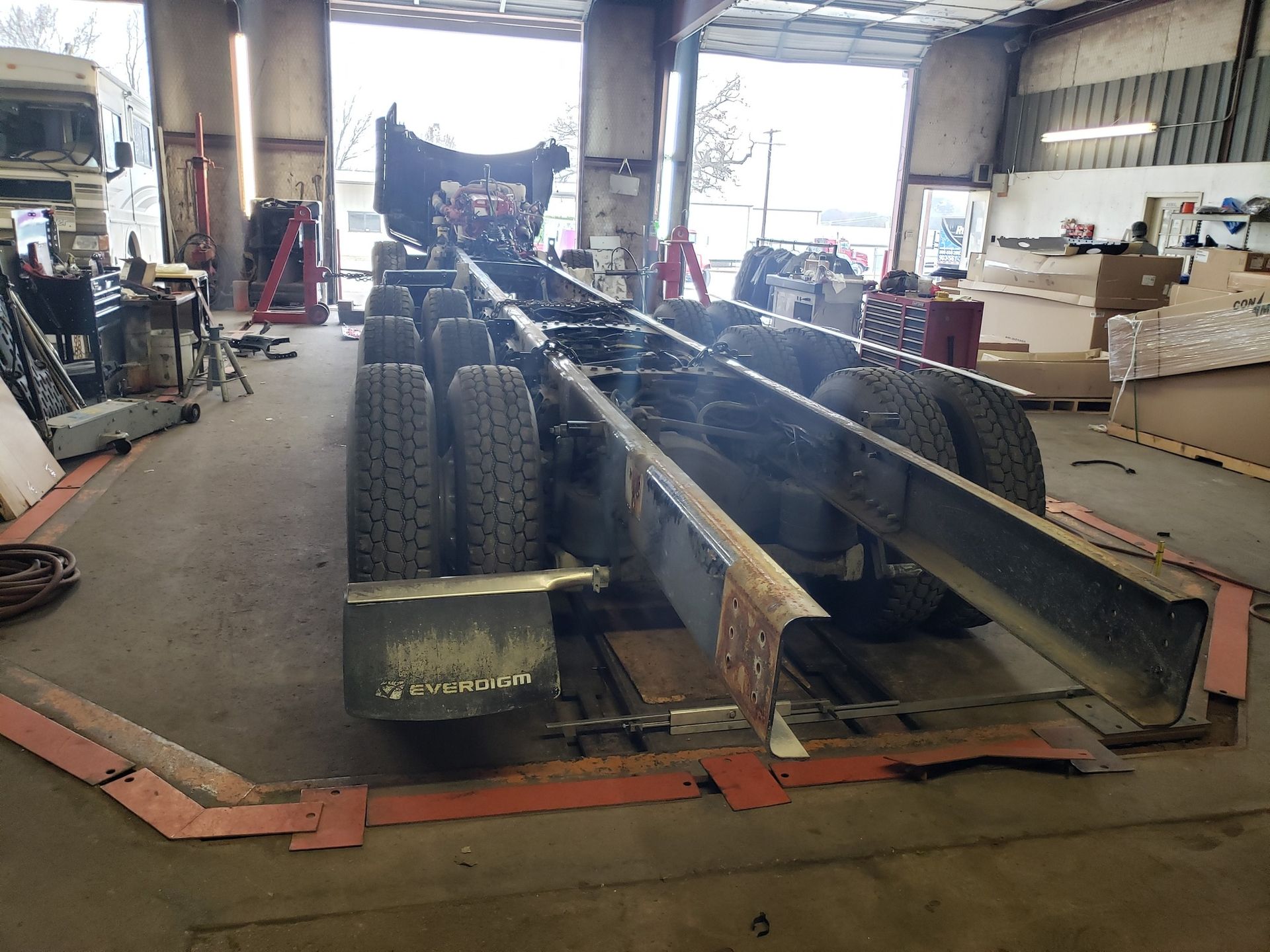 Truck chassis in a repair shop, showing tires, frame, and equipment.