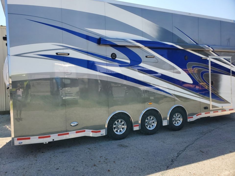 Silver and blue race car trailer with three axles parked outside.