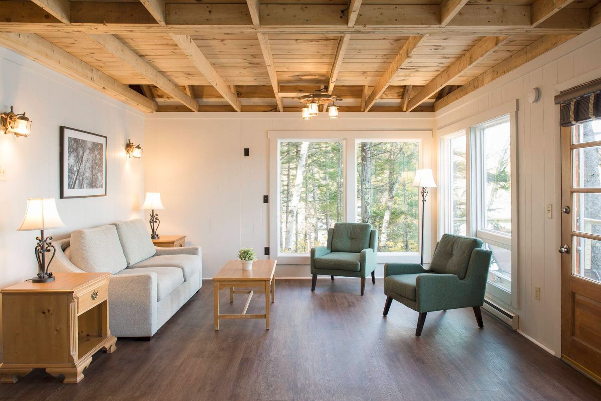 Living room with light gray sofa, two green armchairs, wooden coffee table, and large windows with a view.