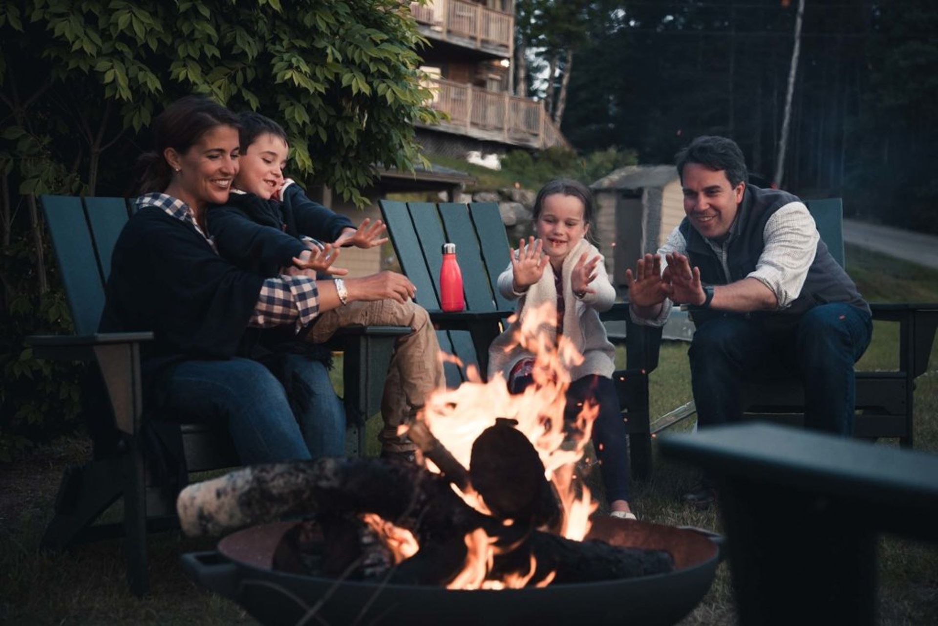 Family warms hands near a campfire in a backyard.