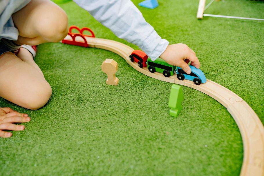 A child plays with a wooden toy train on a curved track set on a green surface.
