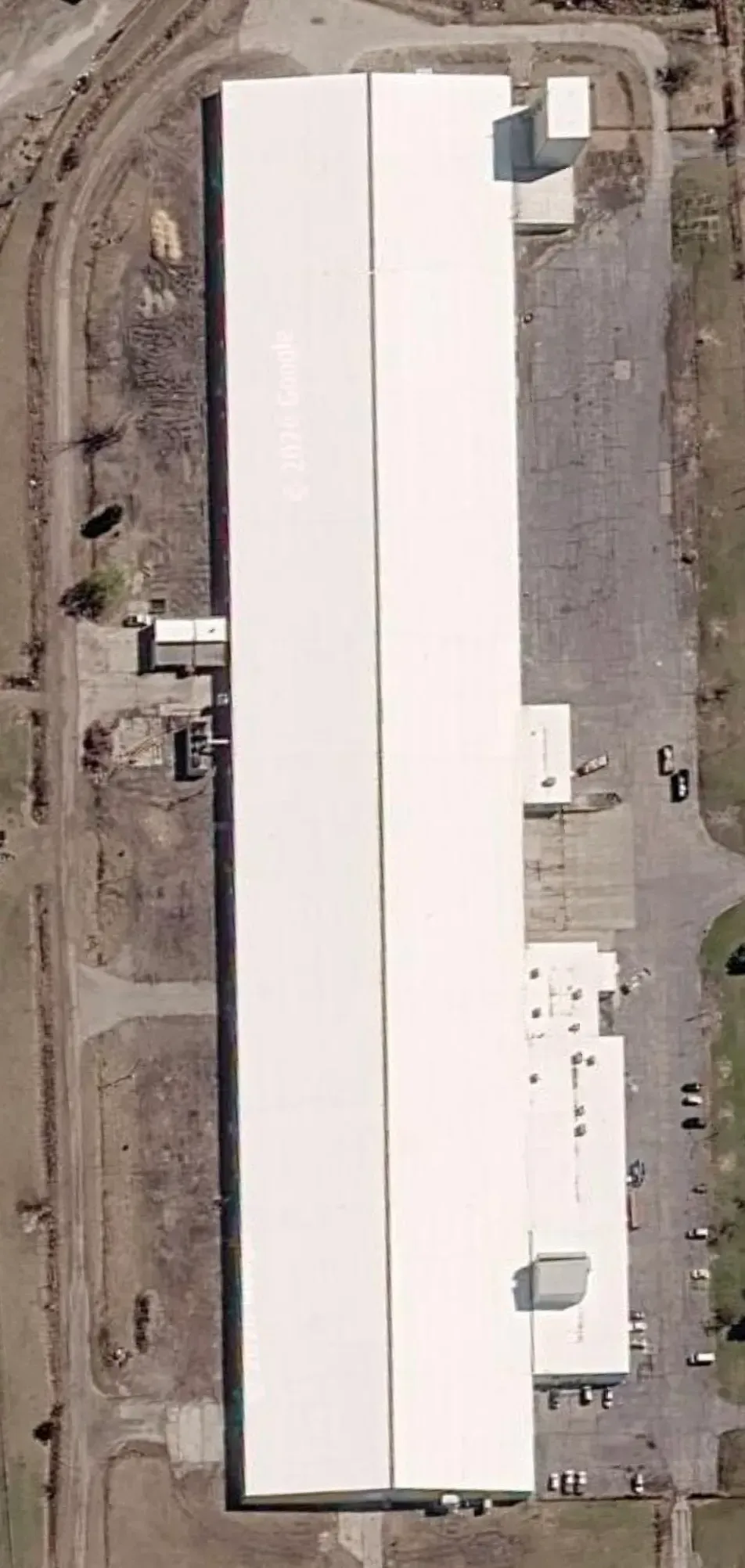 Aerial view of a large white-roofed industrial warehouse in a gravel lot.