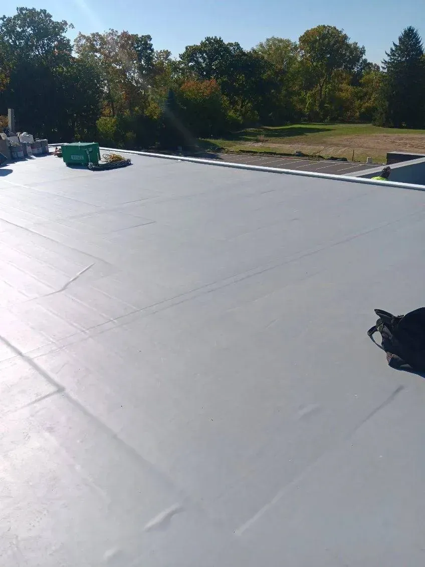 Large white rooftop with trees and blue sky in the background, viewed in bright sunlight