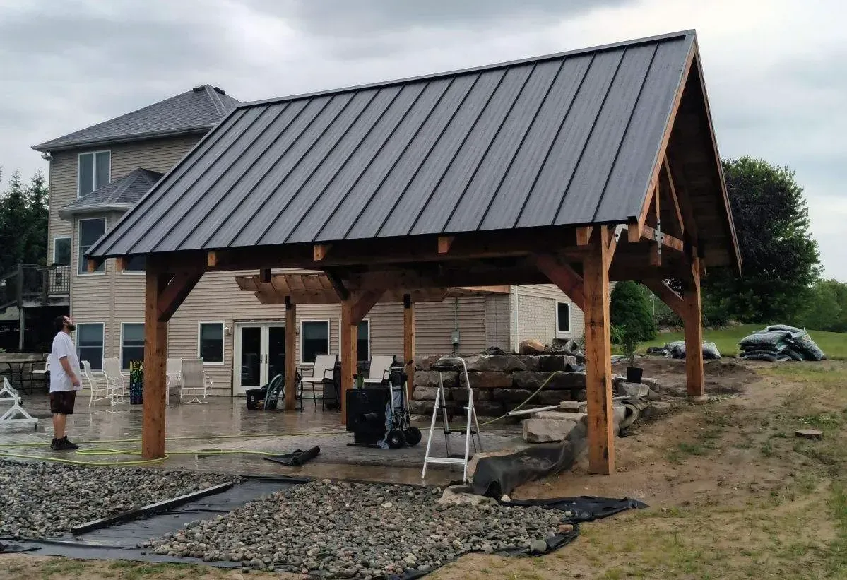 Wooden pavilion with metal roof under construction beside a house and gravel path