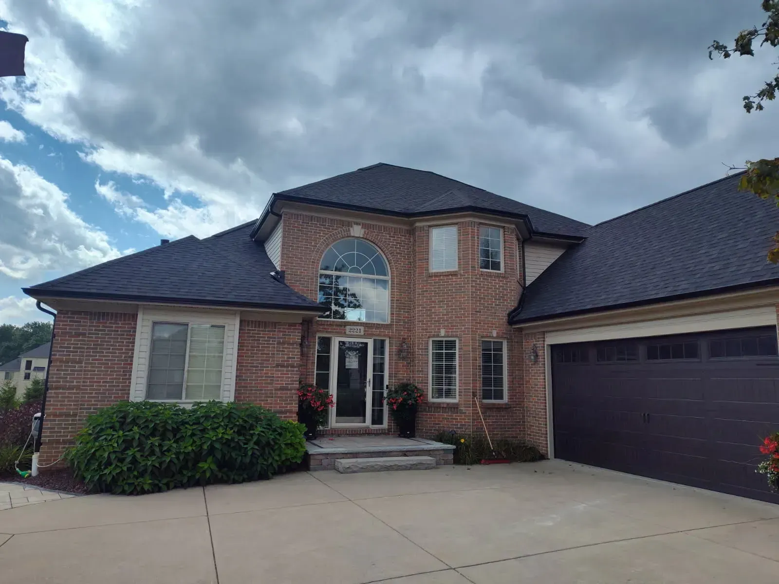 Two-story brick house with arched window, dark roof, and attached garage under cloudy sky