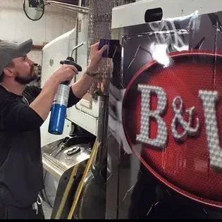 Shop owner Joel reviewing a finished vehicle wrap on a truck with a customer inside the Burleson shop