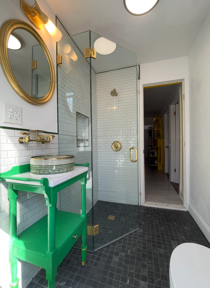 Frameless shower door with brushed gold hardware beside a green vanity