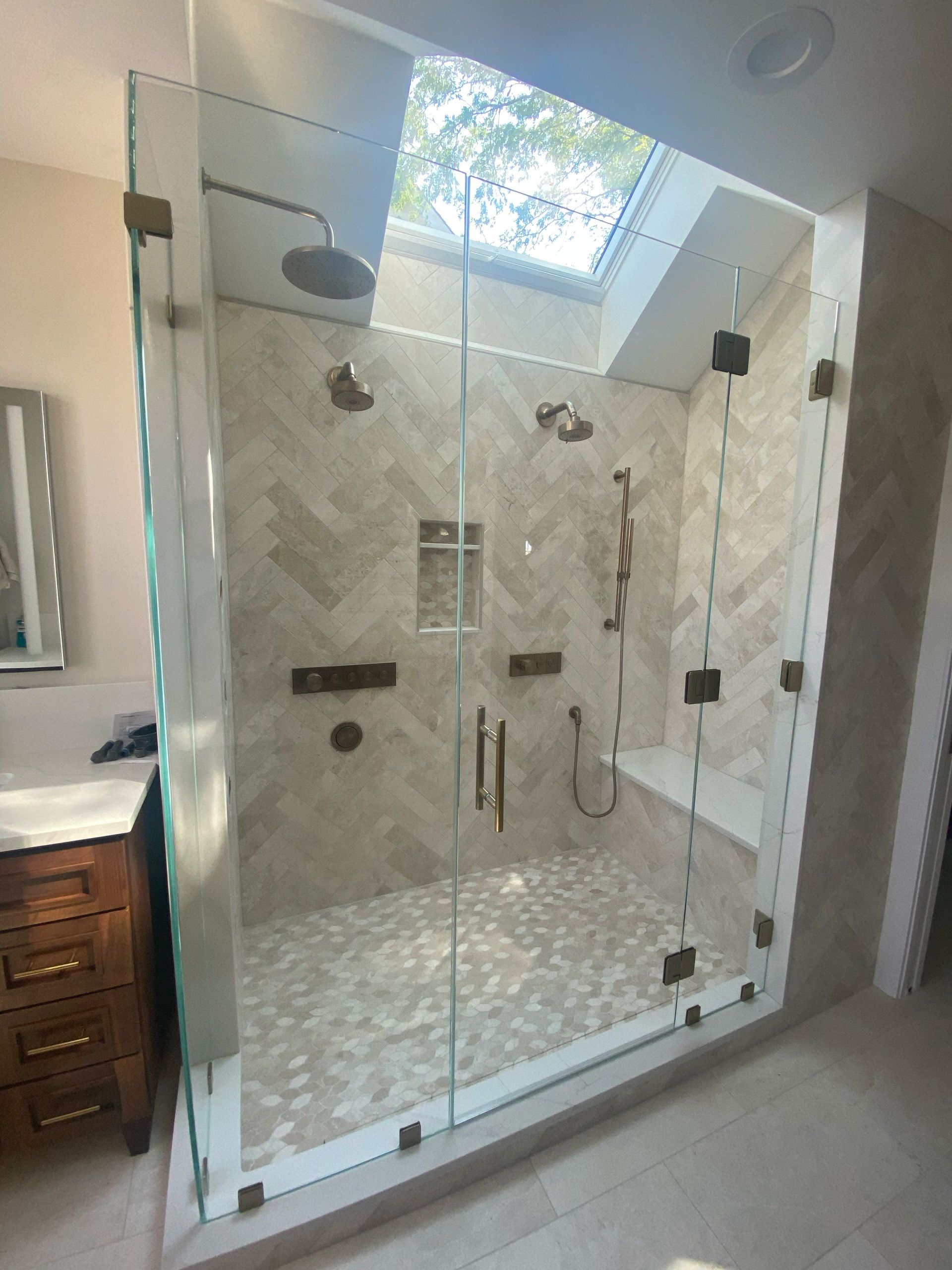 Frameless glass shower with bronze hardware under a skylight
