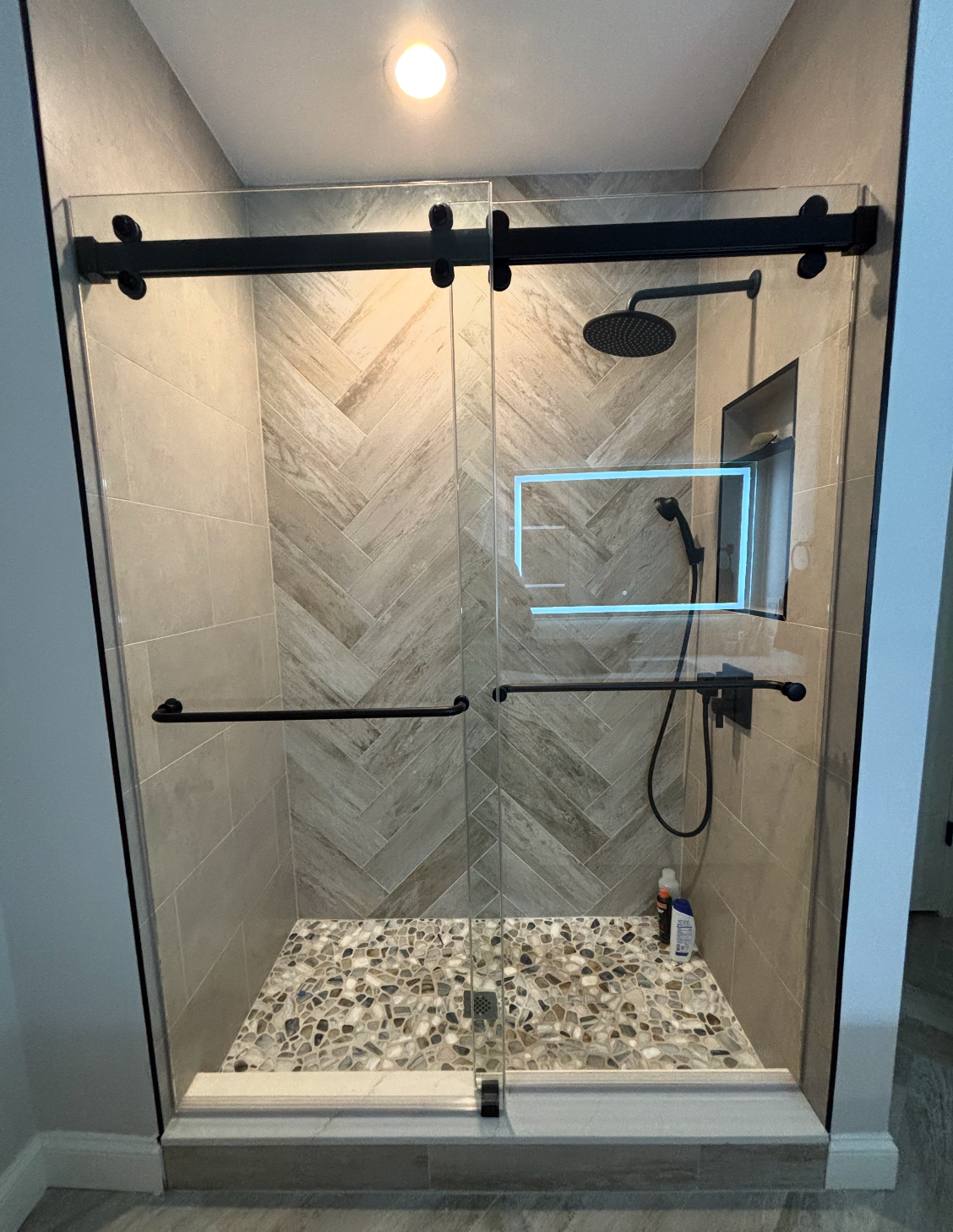 Matte black sliding shower door over a pebble shower floor