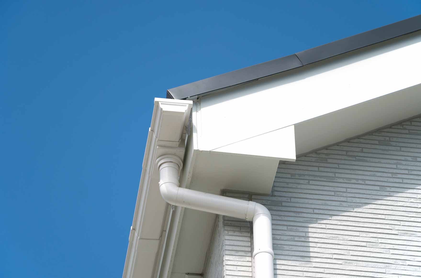 White house roof and gutter against a clear blue sky