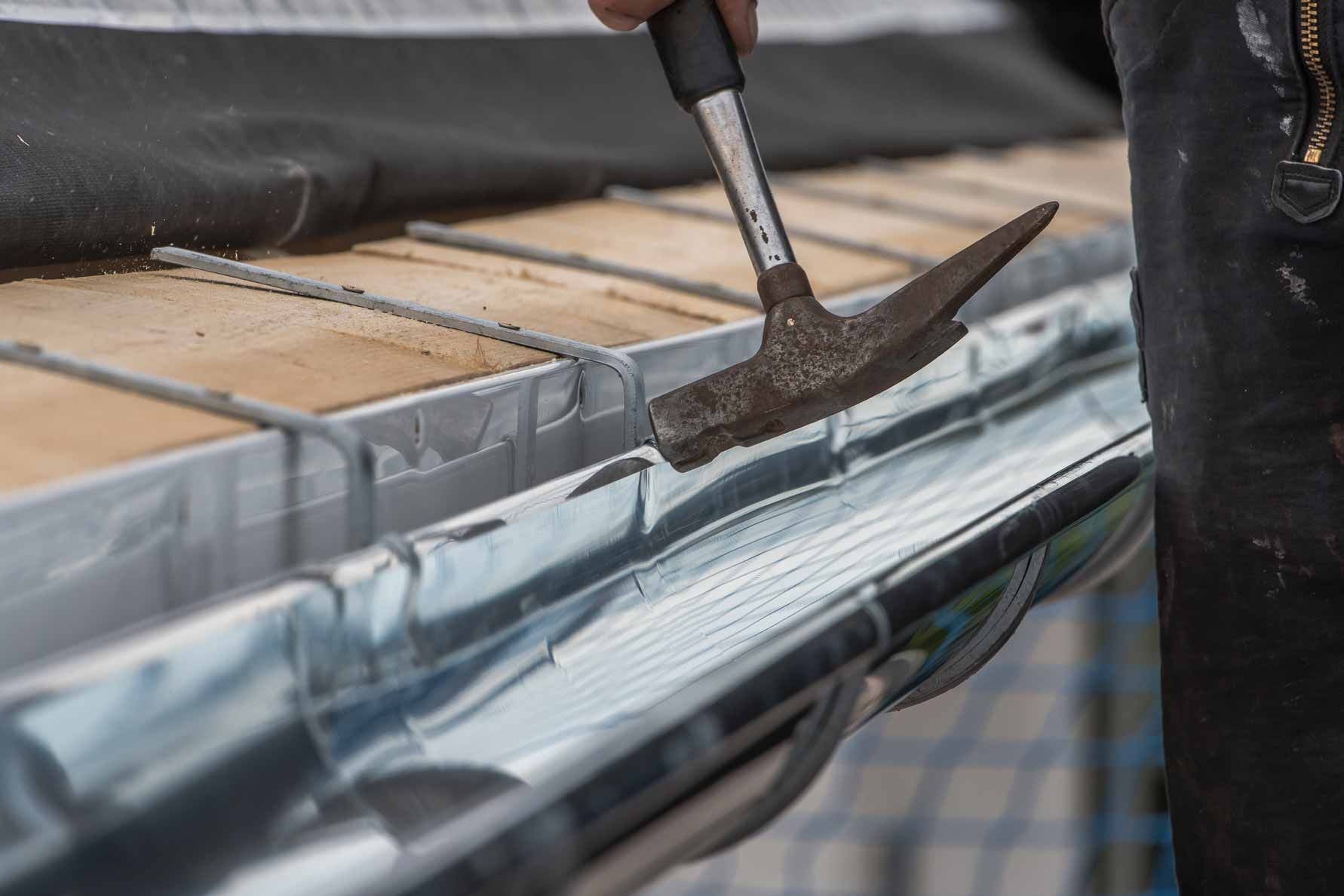 Hammer repairing a metal gutter on a roof