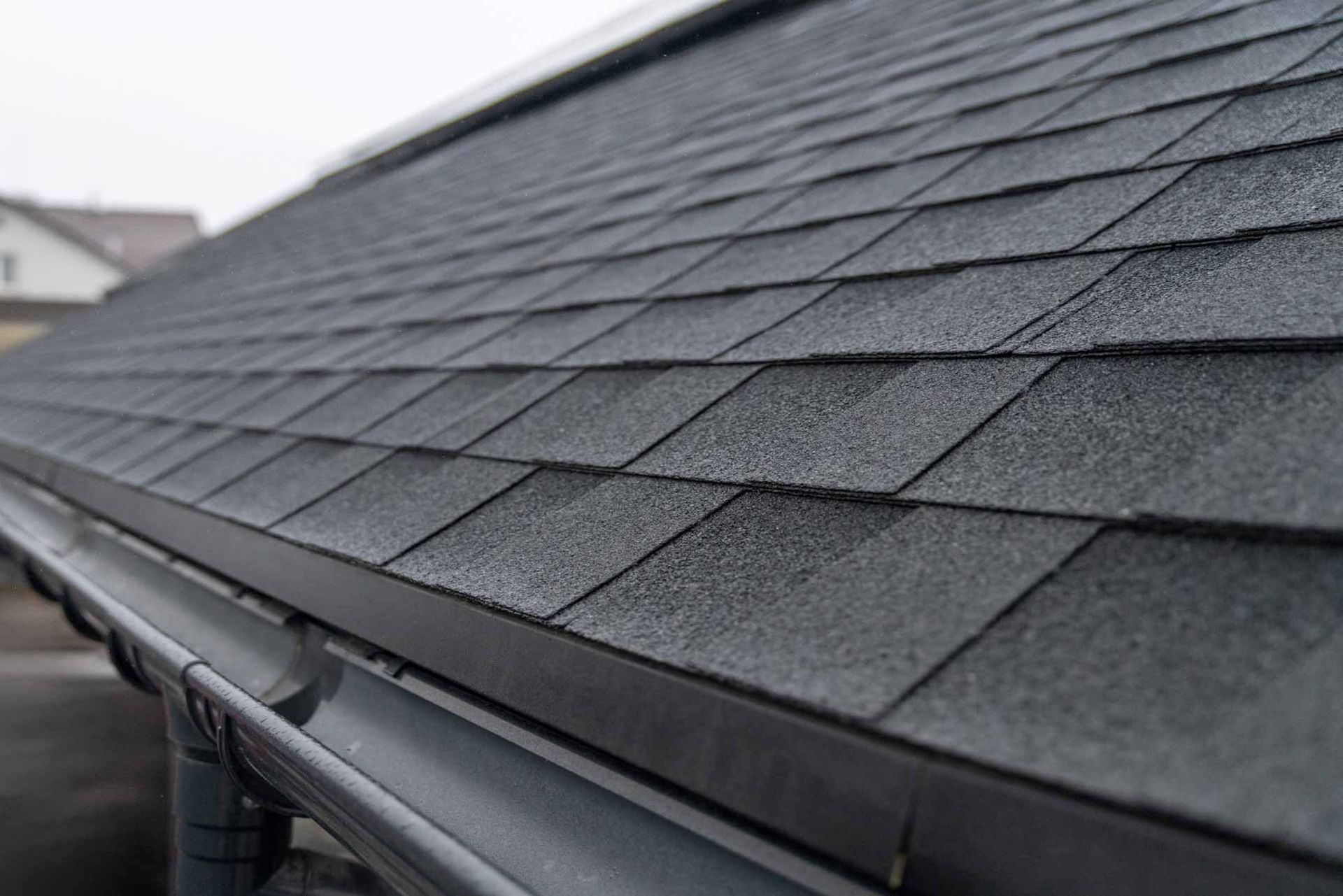 Close-up of a dark gray shingled roof with a gutter along the edge
