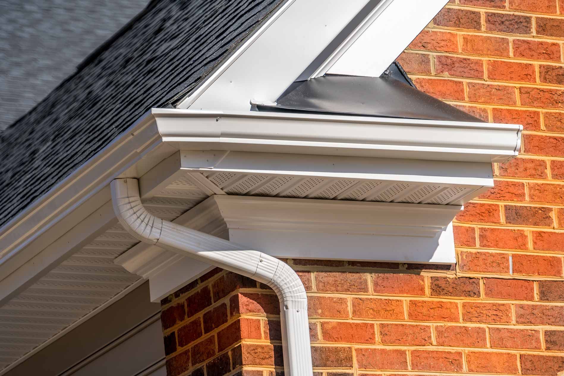 White gutter and downspout on a brick house roof corner