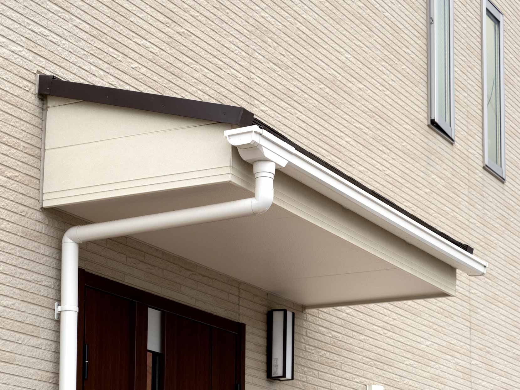 White awning over a building entrance with a downspout and beige brick wall