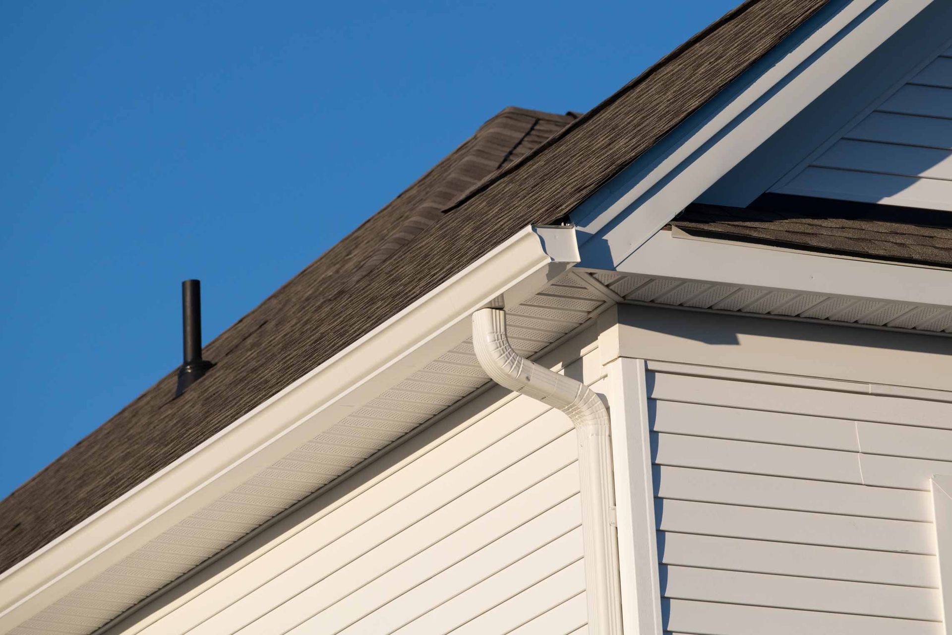 White house roof eave with gutters and downspout against blue sky