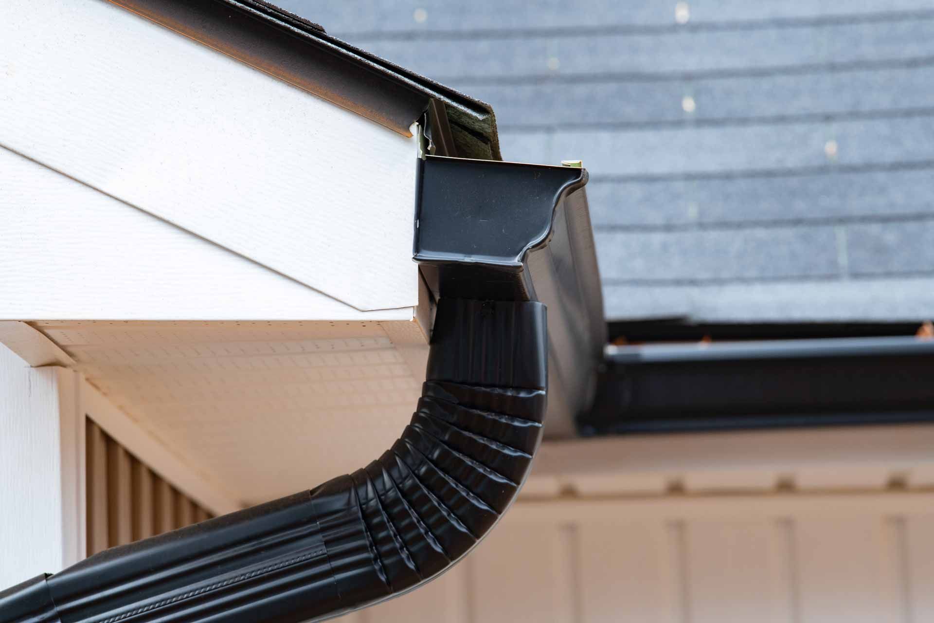Black gutter downspout attached to a white house roof edge