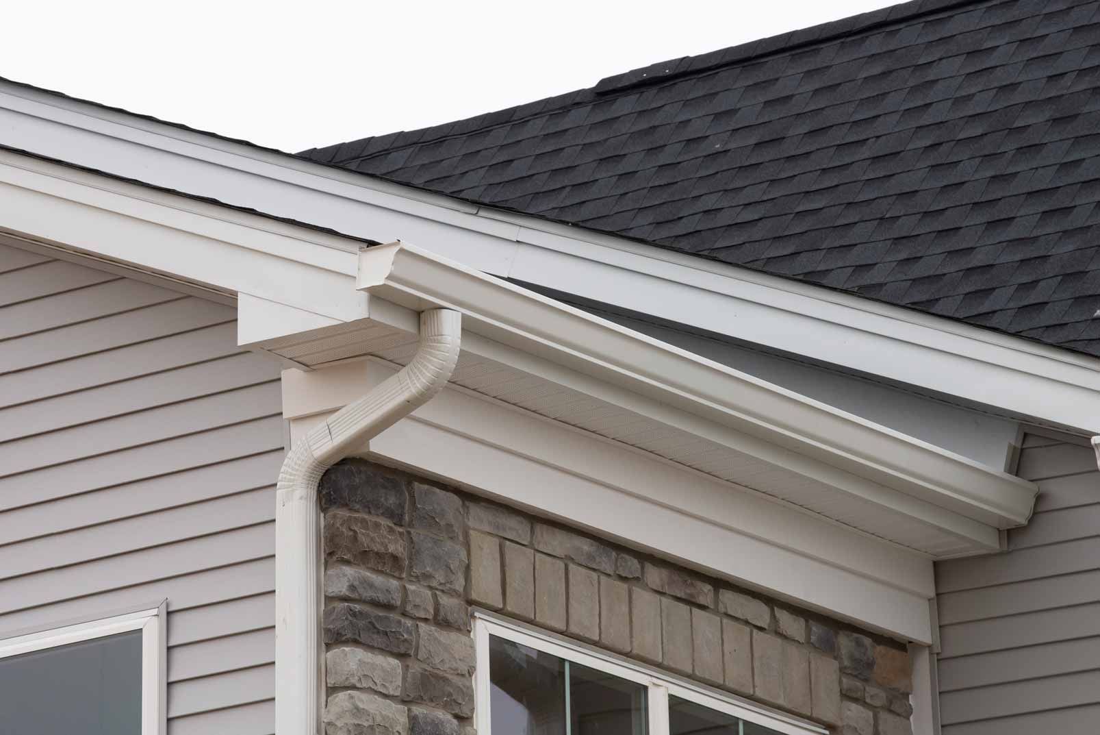 Close-up of a house roof, white gutter, and stone-and-siding exterior wall