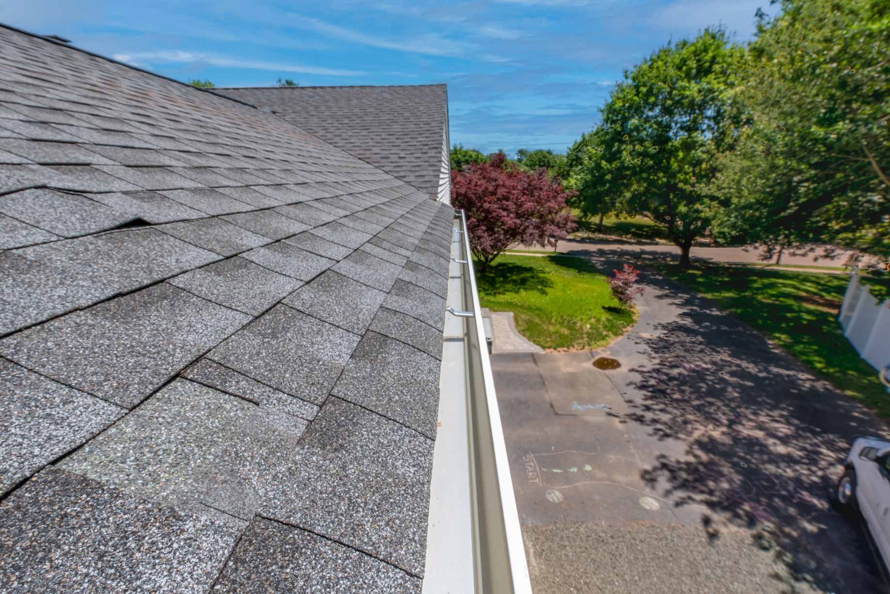 Rooftop with gray shingles overlooking a driveway, green trees, and a blue sky