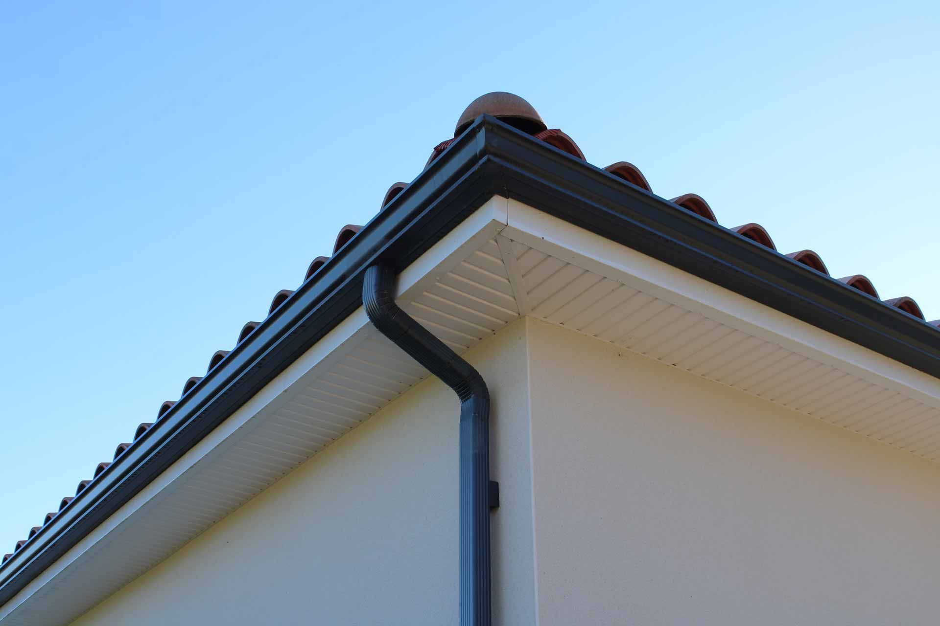 Close-up of a house roof corner with dark gutters against a blue sky