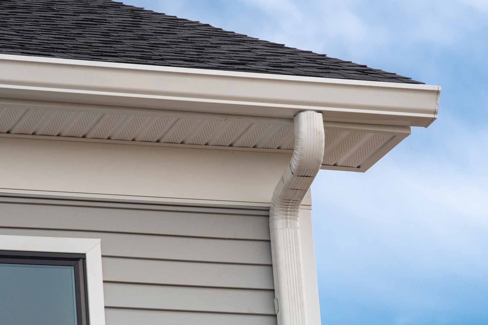 White house eave with gutter downspout and gray siding against a blue sky