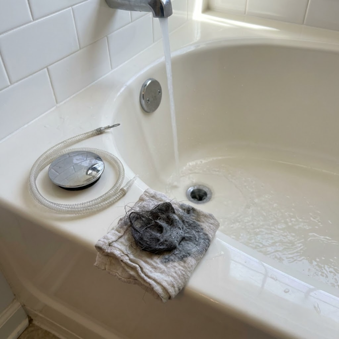 Bathtub corner with a towel holding a pile of dark hair and a metal drain cover nearby