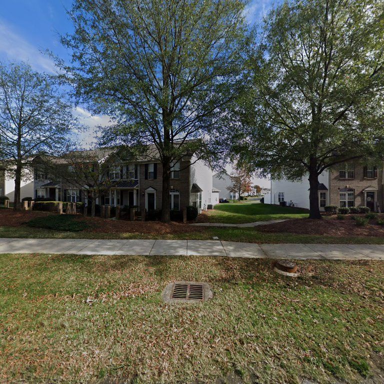 Apartment buildings with trees, a sidewalk, and a grassy lawn under a partly cloudy sky