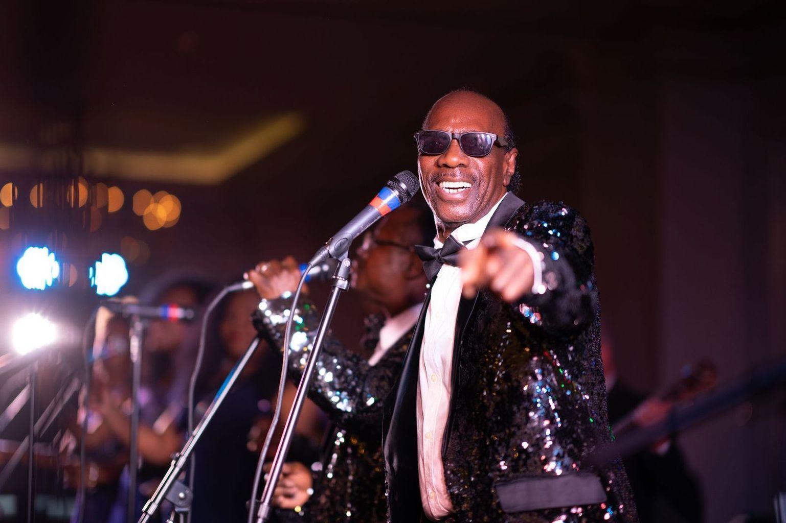 A man in a tuxedo is singing into a microphone while wearing sunglasses.
