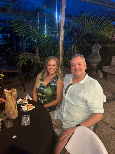 Smiling couple seated at an outdoor dinner table at night with palm trees in the background