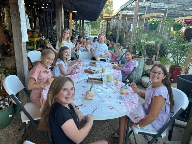 Group seated around a long outdoor table at a restaurant, smiling and chatting over drinks and plates