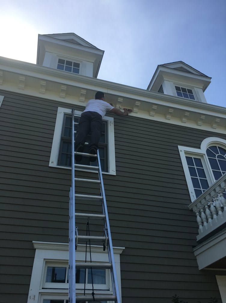 Person on ladder working on a house roof and upper window