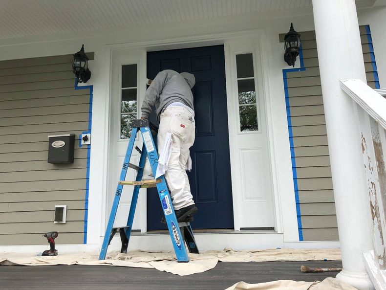 Person on a blue ladder painting a front door on a house porch