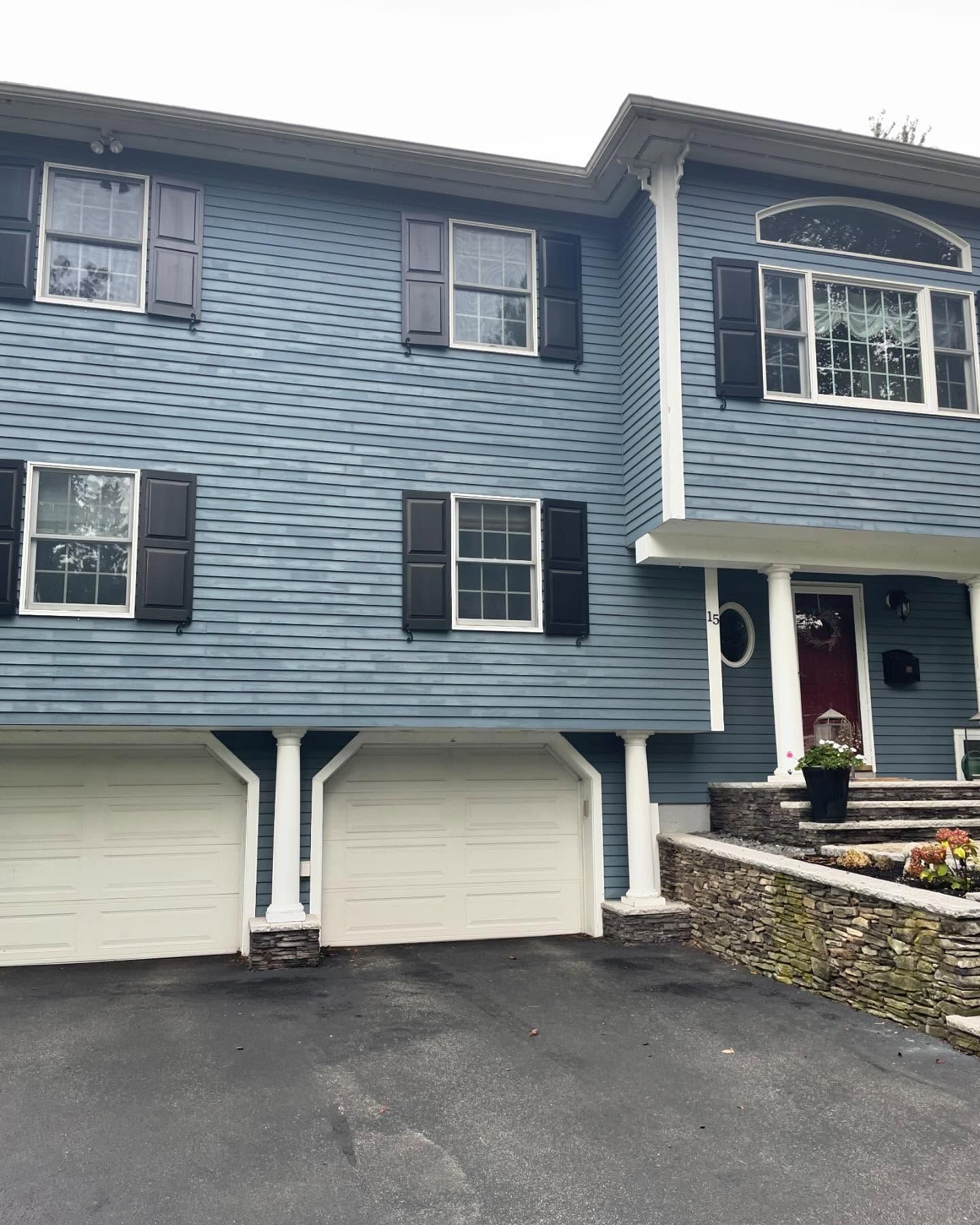 Blue two-story house with white trim, garage doors, and a front porch by a driveway