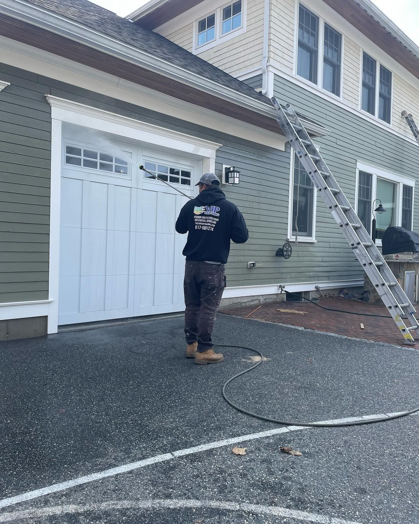 Worker on a ladder repairing the roof and siding of a gray house near a garage.