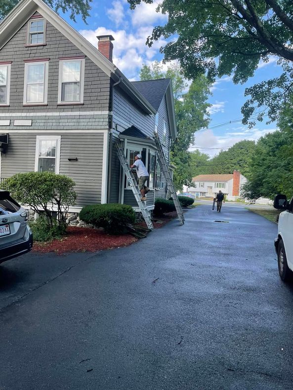 Grey house on a wet driveway with parked cars and a person walking in the distance under a blue sky